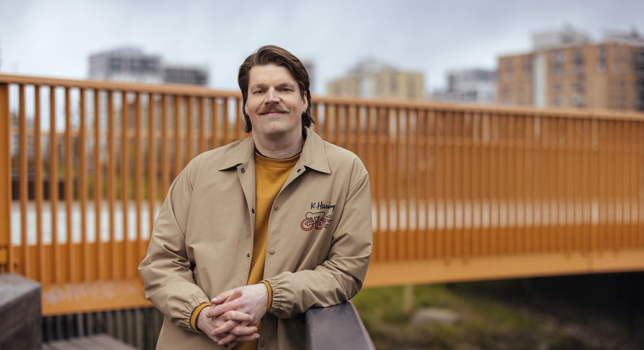 Oranssipaitainen henkilö nojaa kaiteeseen ja hymyilee kameralle.