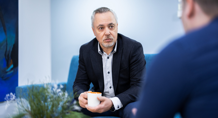 Henkilö keskustelee sohvalla kahvikuppi kädessään keskittyneesti.