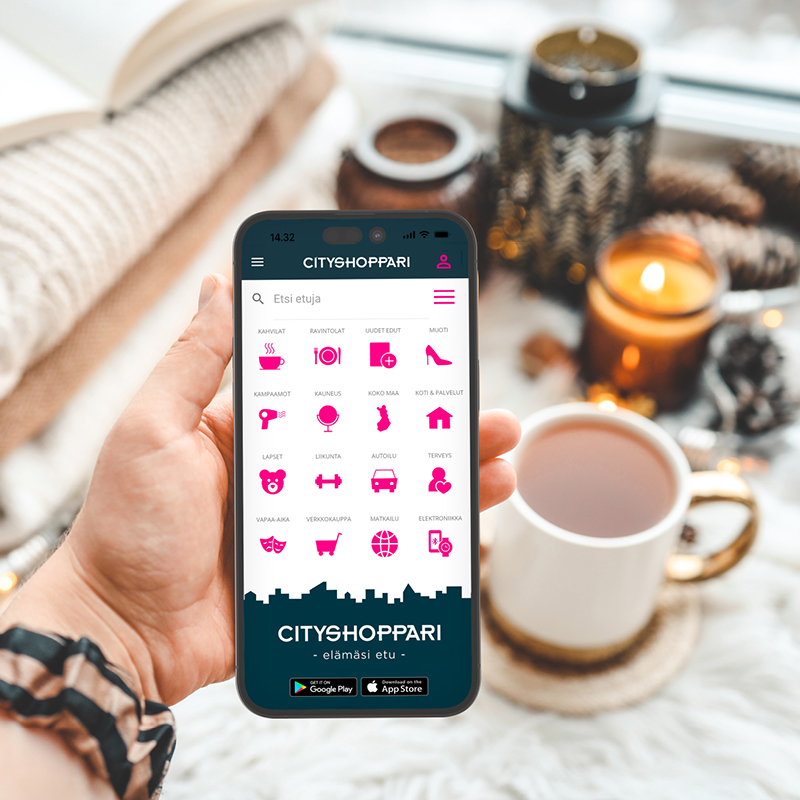 Käsi pitelee puhelinta, jossa on CityShopparin ikonistoa. Taustalla kynttilä ja jouluisia koristeita.