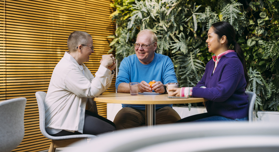 Työntekijät istuvat kahvitauolla avotilassa ja hymyilevät toisilleen.