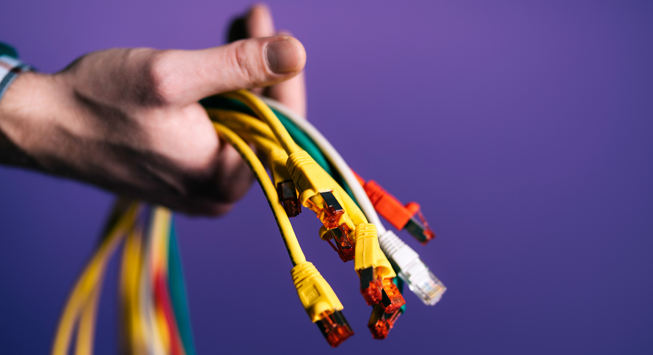 Käsi ja erivärisiä johtoja liilaa taustaa vasten.