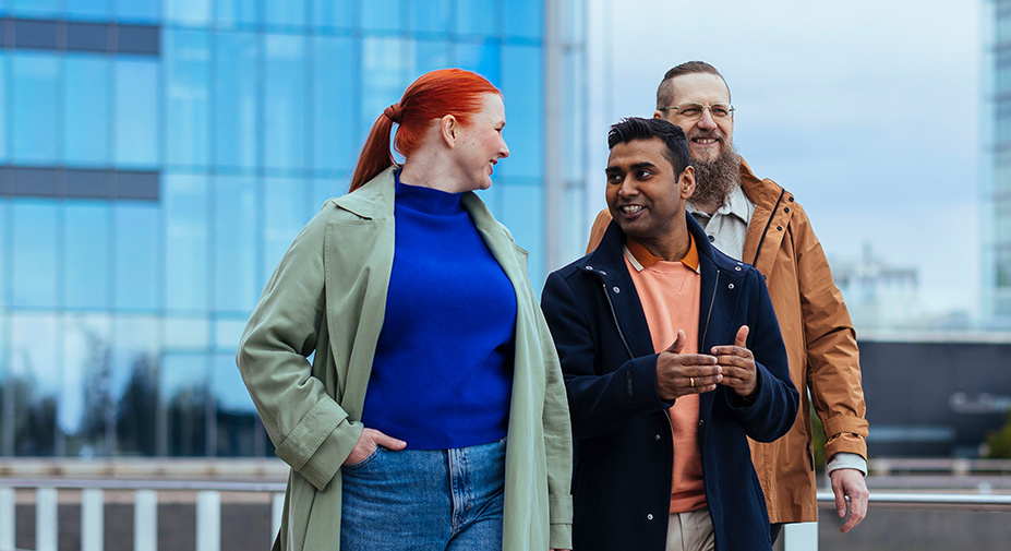 Kolme henkilöä kävelevät veden vierustaa.