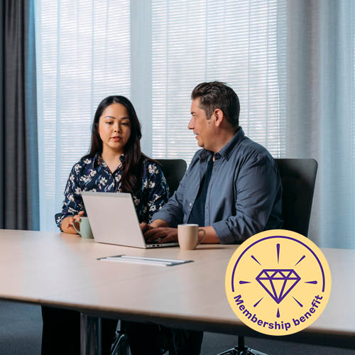 Kaksi toimistotyöntekijää istuu tietokoneen ääressä neuvotteluhuoneessa keskustelemassa. Toisen kädet ovat näppäimistöllä. Pöydällä on kahvikupit.