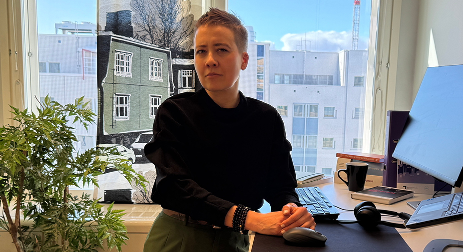 Henkilö nojaa työpöytään ja katsoo kameraan totisesti